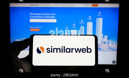 Persona in possesso di un cellulare con il logo della società israeliana di analisi web SimilarWeb Ltd. Sullo schermo davanti alla pagina Web. Concentrarsi sul display del telefono. Foto Stock