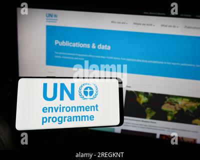 Persona che possiede un telefono cellulare con il logo del programma delle Nazioni Unite per l'ambiente (UNEP) sullo schermo davanti alla pagina Web. Concentrarsi sul display del telefono. Foto Stock