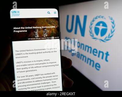 Persona che possiede un telefono cellulare con una pagina Web del programma delle Nazioni Unite per l'ambiente (UNEP) sullo schermo con logo. Concentrarsi sul centro del display del telefono. Foto Stock