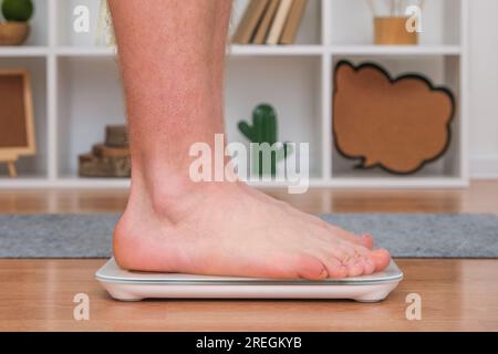 Un uomo si trova sulla bilancia. Il ragazzo sta pesando se stesso. Bilance da pavimento per la salute. Controllo del peso. Foto Stock