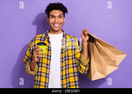 Foto di un ragazzo eccitato e funky che indossa una camicia gialla a quadri, che riceve le offerte di cibo con uno sfondo di colore viola isolato Foto Stock