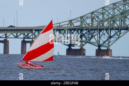 Primo piano di una barca a vela con pesci rossi e bianchi che naviga sulla Great South Bay vicino al ponte che cattura un po' di vento. Foto Stock