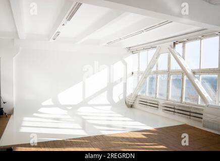Svuotare il grande cyclorama bianco pulito in uno studio fotografico con luce solare e ombre da una grande finestra. Parete semplice studio fotografico vuoto. Foto Stock