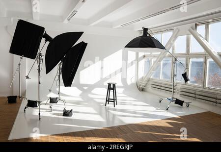 Apparecchiature di illuminazione professionali, libbre, stand, boxeson morbido un enorme e grande cyclorama bianco in un moderno studio fotografico con grandi finestre luminose. Foto Stock