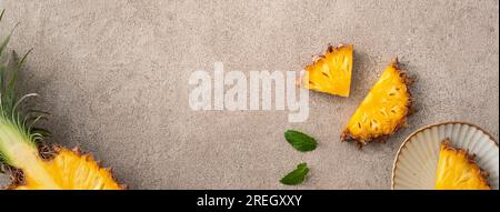 Vista dall'alto del layout dei pezzi di ananas freschi tagliati su sfondo grigio del tavolo, design con frutta tropicale. Foto Stock