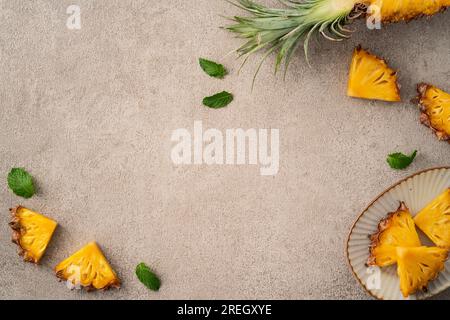 Vista dall'alto del layout dei pezzi di ananas freschi tagliati su sfondo grigio del tavolo, design con frutta tropicale. Foto Stock