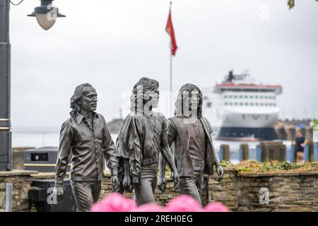 Statua di bronzo sulla passeggiata di Douglas eretta per celebrare i Bee Gees nati sull'Isola di Man. Ammiraglia della Steam Packet Company, Manxman in background Foto Stock