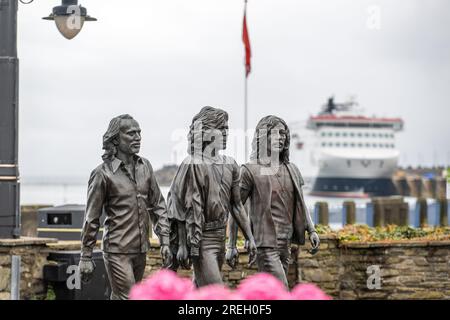 Statua di bronzo sulla passeggiata di Douglas eretta per celebrare i Bee Gees nati sull'Isola di Man. Ammiraglia della Steam Packet Company, Manxman in background Foto Stock