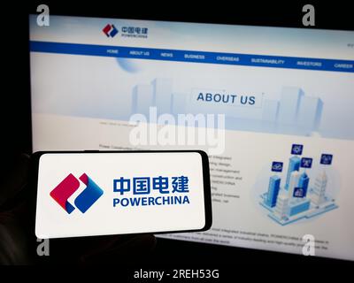 Persona che possiede uno smartphone con il logo della società energetica cinese PowerChina sullo schermo di fronte al sito Web. Concentrarsi sul display del telefono. Foto Stock