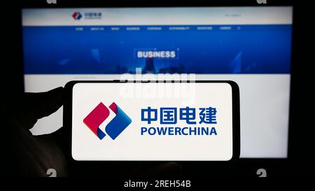 Persona che tiene il cellulare con il logo della società energetica cinese PowerChina sullo schermo di fronte alla pagina Web aziendale. Concentrarsi sul display del telefono. Foto Stock
