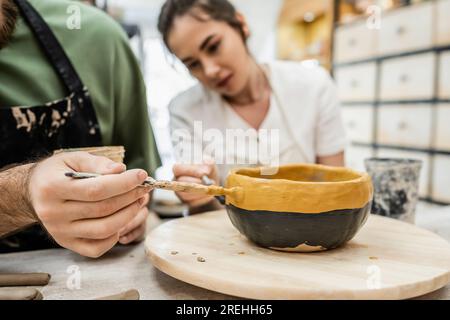 Vista ritagliata di un paio di artigiani che colorano insieme la ciotola in ceramica nello studio di ceramica, banner Foto Stock