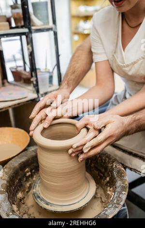 Vista ritagliata dell'argilla che forma vasaio con la sua fidanzata sulla ruota in ceramica nel laboratorio di ceramica Foto Stock