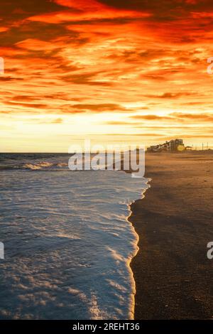 Onde di bianco schiuma di mare lavarsi su una spiaggia alla luce della sera. Foto Stock