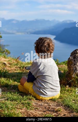 Un bambino visto da dietro che contempla da un punto di vista sopraelevato il lago di Bourget ("Lac du Bourget" in francese) circondato dalle montagne dei dipartimenti Foto Stock