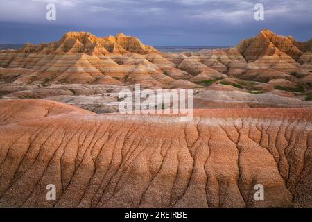 I modelli di erosione evidenziano queste colline in primo piano mentre i temporali primaverili serali si accumulano sulle vette torreggianti della Badlands Nationa del South Dakota Foto Stock