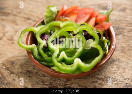 Una ciotola di insalata mista su un tagliere di legno. È composto da peperoni verdi a fette, pomodori e insalata di foglie. Inghilterra Regno Unito GB Foto Stock