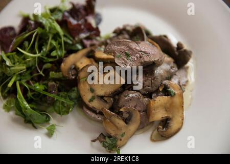 Fegati di pollo britannici fritti e serviti con funghi di castagno importati dalla Polonia, prezzemolo dalla Germania, basilico dall'Etiopia e catrame Foto Stock