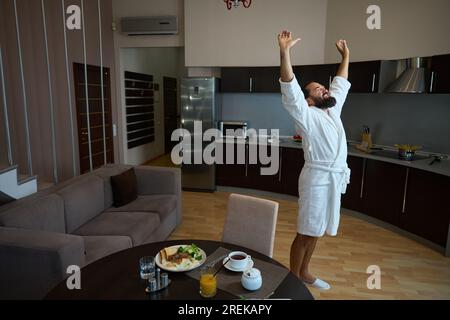 Il maschio in accappatoio si gode la mattina in camera d'hotel Foto Stock