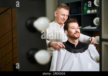 Il barbiere diligente serve clienti maschi in un moderno salone Foto Stock