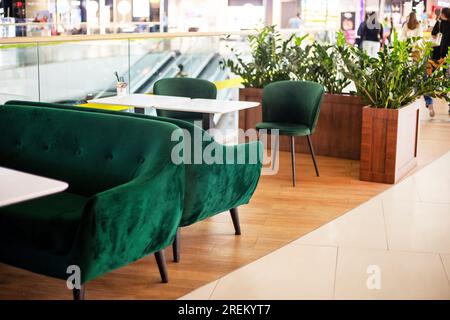 interni con poltrone rivestite di velluto verde con tavoli bianchi in un caffè in un centro commerciale Foto Stock