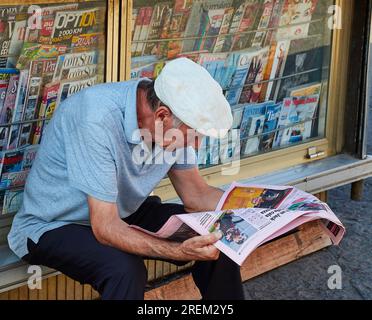 Uomo anziano seduto di fronte al chiosco che legge un quotidiano, cappello bianco, città vecchia, Catania, costa orientale, Sicilia, Italia Foto Stock