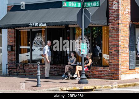 Prattville, Alabama, USA - 16 giugno 2023: Due donne con un cane che chiacchiera con un uomo più anziano di fronte al West Main Coffeehouse e al Creamery nel centro storico Foto Stock