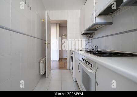 Cucina arredata su un lato della stanza con mobili bianchi con piano di lavoro dello stesso colore ed elettrodomestici integrati Foto Stock