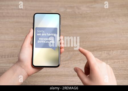 Donna ha ricevuto un messaggio Scusate le difficoltà tecniche sullo smartphone al tavolo di legno, primo piano Foto Stock