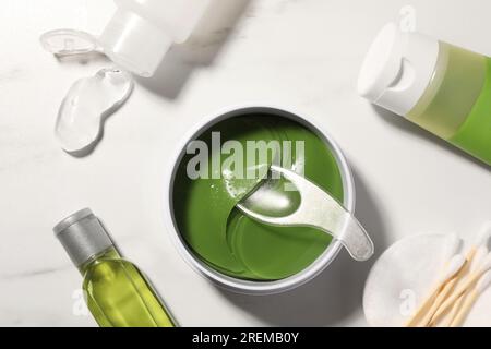 Barattolo di cerotti oculari con cucchiaio e prodotti cosmetici su un tavolo in marmo bianco, posizionamento piatto Foto Stock
