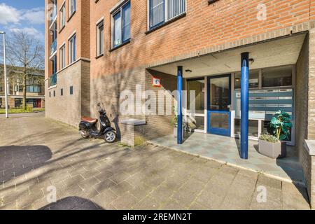 una motocicletta parcheggiata di fronte ad un edificio in mattoni con porte e finestre blu su entrambi i lati dell'edificio è un parcheggio vuoto Foto Stock