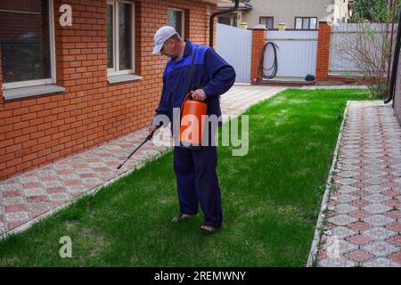 Un uomo lavora in giardino, spruzzando le erbacce da uno spruzzatore. Foto Stock
