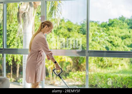 La giovane donna incinta ama pulire la sua casa. Facile pulizia con un aspirapolvere wireless. Donna incinta che pulisce il pavimento con l'aspirapolvere portatile Foto Stock