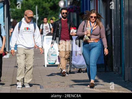 Bella giovane donna che indossa jeans in denim, vestita alla moda, cammina in città trafficata con drink da asporto, con borsa a spalla, in estate, Regno Unito. Foto Stock