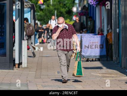 Uomo che cammina, vestito in modo intelligente con camicia e pantaloni abbottonati, che usa fazzoletti o fazzoletti per pulire il naso, forse febbre da fieno o freddo, estate nel Regno Unito. Foto Stock