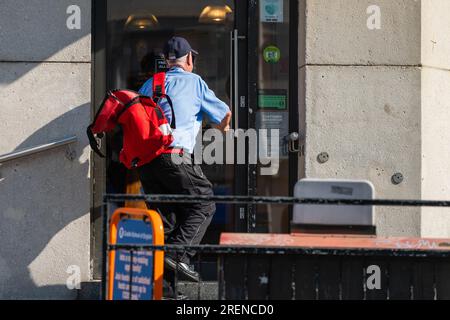 Royal mail Postman o Post Person che consegna lettere e posta a locali aziendali in un'area urbana in Inghilterra, Regno Unito. Occupazione. Foto Stock