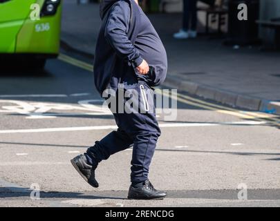 Uomo in sovrappeso con pancia grande o pancia grande, senza mostrare la testa, camminando attraverso una strada, Regno Unito. Uomo obeso. Foto Stock