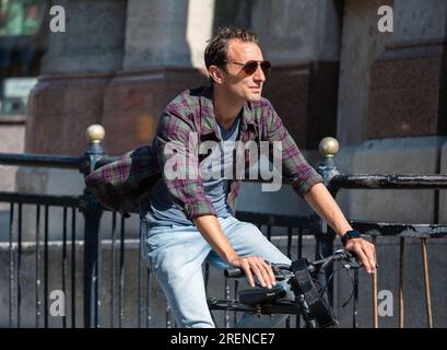Giovane ciclista maschile, giovane in bicicletta su strada in una città frenetica d'estate, senza indossare il casco, in Inghilterra, Regno Unito. Stile di vita sano. Foto Stock
