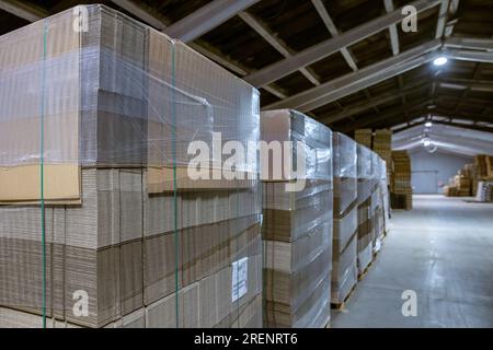 Scatole di cartone pieghevoli. Fogli perforati di cartone ondulato impilati su pallet. Imballaggio di prodotti finiti nella produzione industriale. Foto Stock