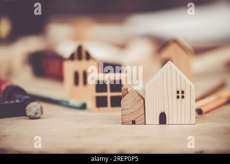 piccola e grande casa in legno sul tavolo da costruzione con gli strumenti per costruire un nuovo concetto di confronto delle dimensioni della scala domestica. Foto Stock