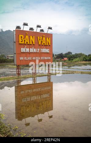 Un grande cartello rosso con luci di lettura si riflette nelle risaie in quanto pubblicizza il villaggio Van della minoranza etnica thailandese bianca a mai Chau, in Vietnam, come un Foto Stock