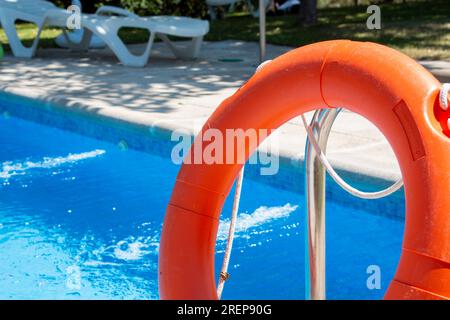 Galleggiante di salvataggio arancione poggiato sulla scala di acciaio di una piscina Foto Stock