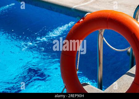 Galleggiante di salvataggio arancione poggiato sulla scala di acciaio di una piscina Foto Stock