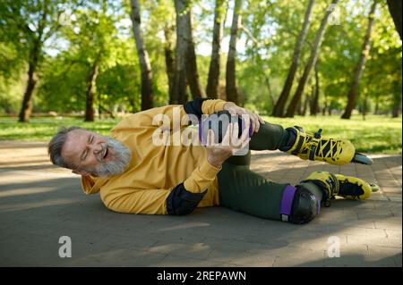 L'uomo anziano sente dolore quando il ginocchio cade mentre pattina nel parco Foto Stock