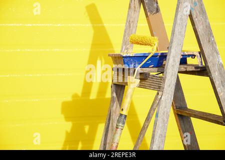 Verniciare gli attrezzi con la scala contro una parete gialla appena verniciata Foto Stock