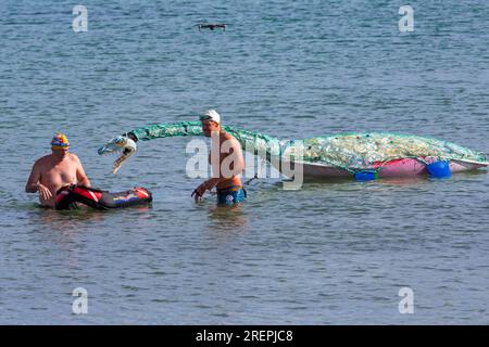 Swanage, Dorset, Regno Unito. 29 luglio 2023. Percy Searonster il modello di dinosauro plesiosauro realizzato con 600 bottiglie di plastica del peso di 60-65kg creato dalle sculture di Glenn Martin viene trainato lungo Swanage Bay dal nuotatore Oly Rush e da altri nuotatori. Una nuotata di 12 ore per Oly, parte del suo intenso programma di allenamento per il suo tentativo di record mondiale, 30 ore di nuoto intorno alla splendida isola di Itaca, in Grecia, a settembre. Con l'obiettivo di aumentare la consapevolezza circa gli impatti devastanti dell'inquinamento plastico, nonché i fondi per il progetto Planet Earth e Healthy Seas. Crediti: Carolyn Jenkins/Alamy Live News Foto Stock