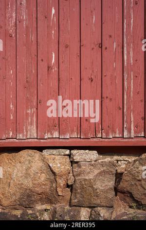 Parete in legno rosso e fondazione in pietra di una vecchia casa a Loviisa, Finlandia. Foto Stock