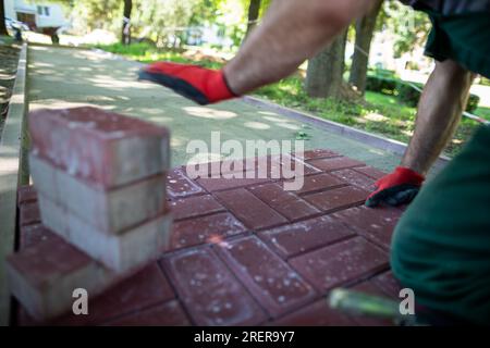 Un operaio edile si inginocchia per posare pietre pavimentate in una giornata di sole. Foto Stock