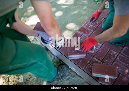 Un lavoratore inserisce le pietre di pavimentazione e l'altro le poggia in modo uniforme e preciso. Foto Stock