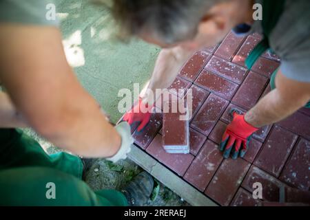 Un lavoratore inserisce le pietre di pavimentazione e l'altro le poggia in modo uniforme e preciso. Foto Stock