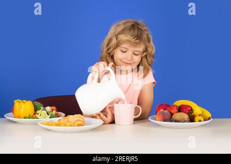 Capretto che versa latte intero di mucche. Ritratto di bambino mangiare cibo fresco sano in cucina a casa. Bambino che mangia la colazione prima della scuola. Foto Stock